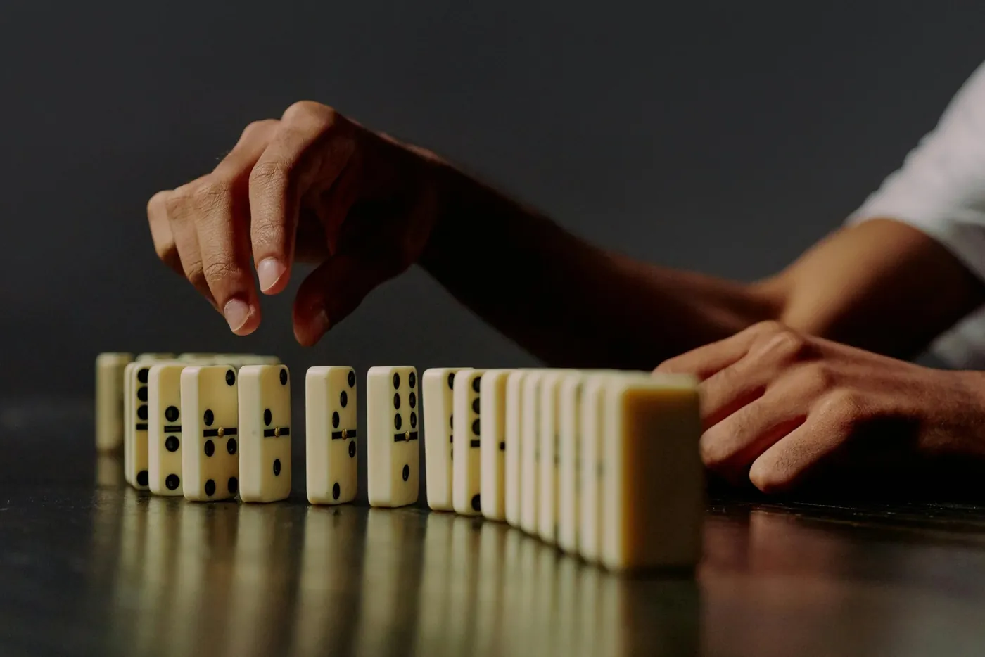 A hand stopping a falling line of dominoes before the rest topple