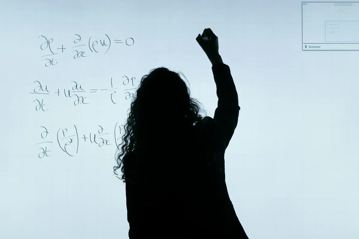 A silhouetted figure working through equations on a whiteboard